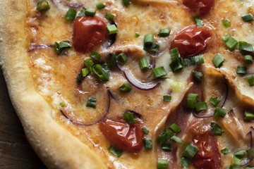 Prosciutto pizza with meat, cheese, dried tomatoes, spring onions and bread on a wood surface