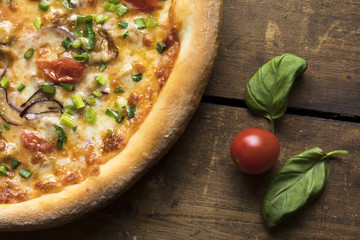 A pizza with shiitake mushrooms, spring onions, cheese, dried tomatoes on a vintage wood surface