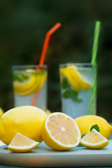 Organic, ripe lemons on blue board. Fresh lemonades or mojito cocktails in two glasses with straws in background.