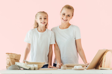 beautiful mother and daughter in white t-shirts looking at camera while cooking together isolated...