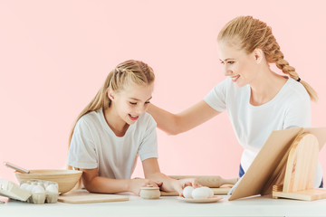 happy young mother and daughter in white t-shirts cooking together isolated on pink