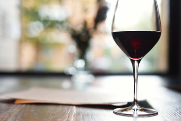 A Glass of red wine in restaurant or cafe on wooden table in front of window, romantic date, lunch relaxation