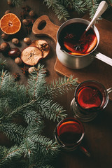 Fototapeta na wymiar hot mulled wine in saucepan and glass cups with spices on wooden background with fir branches