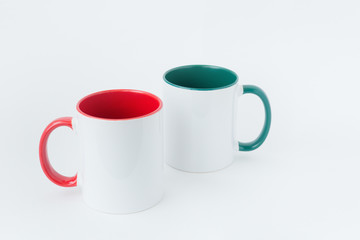 Two white mugs, with a green and red handle on a light background. 