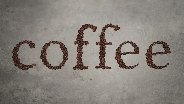 Hands full of brown coffee beans. 
The coffee beans contain a coffee inscription. Top view on food ingredients, stop motion.