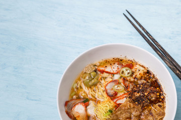 Closeup egg noodle soup with grill pork in white bowl on blue table background, Thai style spicy noodle soup
