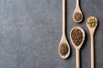 top view of wooden spoons with dried aromatic seasonings on grey background