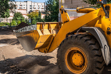yellow loader with bucket loaded by gravel at construction site