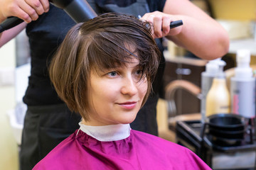 Beautiful young woman in hairstyle salon getting bob haircut