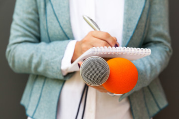 Journalist at news conference, holding microphone, writing notes