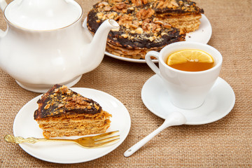 Cup of tea, porcelain teapot and homemade chocolate puff cake on white plate