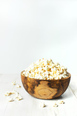 Fototapeta na wymiar Brown wooden bowl with delicious traditional popcorn on a light wooden background. Top view of a light meal background.