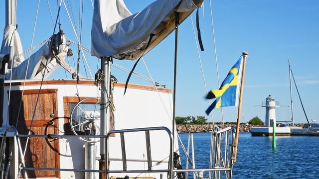 Swedish flag blowing in the wind on a vintage sailing boat. Lighthouse in the background. Location lake Vattern in Granna, Sweden.