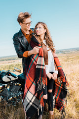 young couple in glasses standing near vintage motorbike and looking at each other