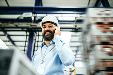 A portrait of an industrial man engineer with smartphone in a factory.