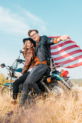 Fototapeta premium young smiling couple with american flag sitting on motorbike, independence day concept