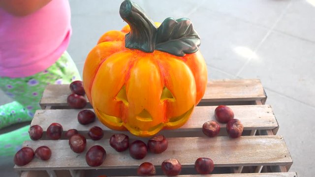 Two little girls playing feeding chestnuts to halloween pumpkin, child play, holiday decoration, faces unrecognizable