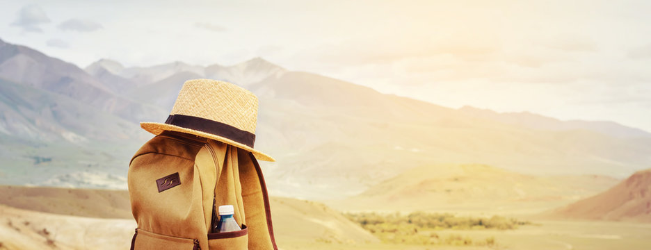 Hipster backpack, bottle of water and straw hat on hill in mountains. Active travel concept.