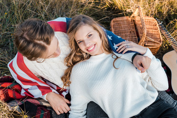 attractive couple with american flag relaxing on grass, independence day concept