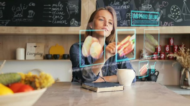 Blonde pretty woman in the kitchen uses transparent hologram futuristic screen to purchase vegetables online, future shopping concept