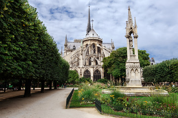 Fototapeta na wymiar Paris, France - August 13, 2017. Medieval Notre Dame de Paris, most visited french monument of Gothic architecture. View from Square Jean XXIII - park with Virgin Fountain and flowers near Cathedral.