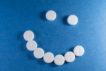 Happy smile made from white pills on blue background