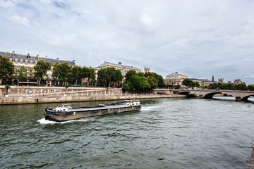 Obraz premium Paris, France - August 16, 2017. View of medieval Cite island and Pont au Change bridge from Seine riverside. Popular french landmark and tourist cruise boat in river Seine.