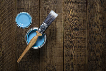 Can of pastel blue paint with brush on wooden floorboards.