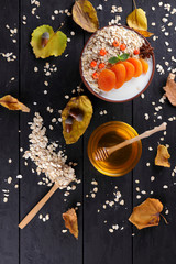 Oatmeal with dried apricots and honey on black background. Oat flakes with milk and green mint on dark wooden boards. Healthy food for vegans. Dry oats with berries of mountain ash. Autumn pattern