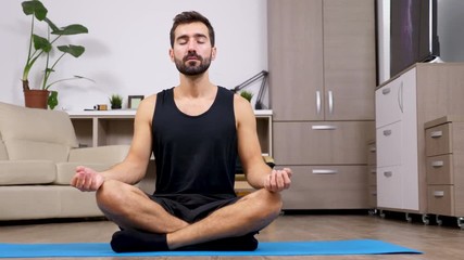 Man at home practicing yoga in the living room. He sitts in the lotus pose meditates. Dolly slider 4K footage