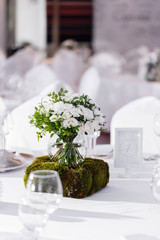 Beautiful and exquisite decoration of the wedding celebration. Flower arrangement of white flowers and blueberry greens, in a glass ball vase