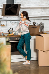 side view of attractive woman talking on smartphone in kitchen with cardboard boxes during relocation in new home