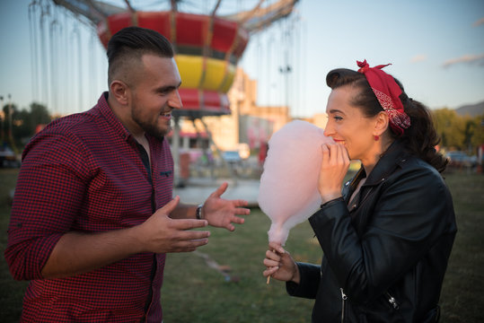young cute  couple  in amusement  park talking and eating cotton candy