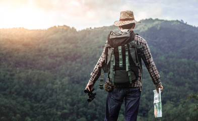hiker with backpack standing holding map and binoculars in hand on the mountain