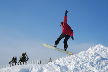 Male snowboarder on the snowy slope on sunny winter day. Young sportsman jumping, spraying...