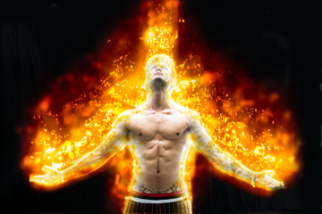 Fototapeta na wymiar Tattooed muscular man with nude torso holding hands apart and burning in fire on black background 