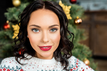 portrait of attractive young woman looking at camera near christmas tree at home