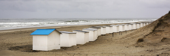 View on the beach huts on the west coast area of Texel. Panoramic view on the North Sea on a day in autumn with beautiful waves and a heavy grey sky, Typical dutch weather in fall.