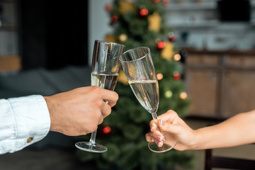 cropped image of couple celebrating christmas and clinking by champagne glasse at home
