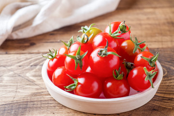 Cherry tomatoes red in ceramic bowl on wooden background