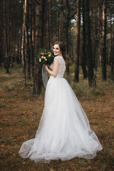 Obraz na płótnie Canvas Beautiful bride in fashion wedding dress on natural background.The stunning young bride is incredibly happy. Wedding day. .A beautiful bride portrait in the forest.