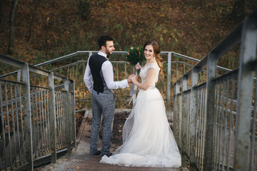 Fototapeta premium Happy young bride and groom descend from the suspension bridge into the forest. wedding photos in an interesting place