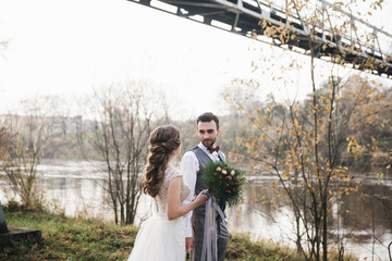 Happy young smiling bride and groom stand near the suspension bridge and the river. Wedding photos...