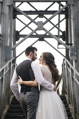 Happy young smiling bride and groom are standing on the suspension bridge. Wedding photos in an interesting place