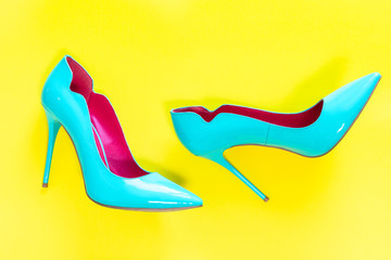 Blue high heels glassy shoes on yellow background, top view