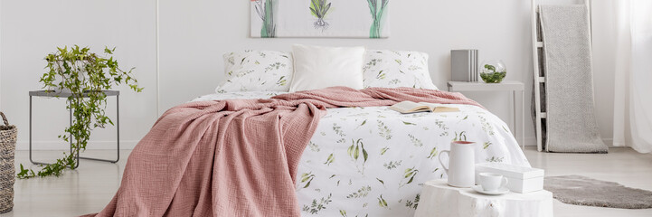 Real photo of a romantic bedroom interior with a pink blanket on a double bed with floral sheets