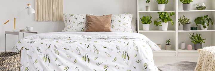 Real photo of a botanical bedroom interior with floral sheets and plants on shelves