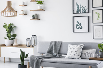 Pillows and blanket on grey couch in white scandinavian loft interior with plants and gallery. Real photo