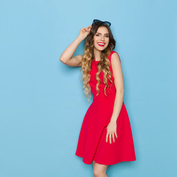 Beautiful Fashion Model In Red Dress Is Looking At Camera And Smiling