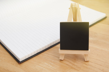 Still life, wooden chalkboard label over opened notebook. Wooden table background. Copy space.